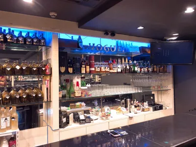 club vogue の店内。青いネオンの VOGUE サインとボトル棚、グラスの並ぶカウンター
