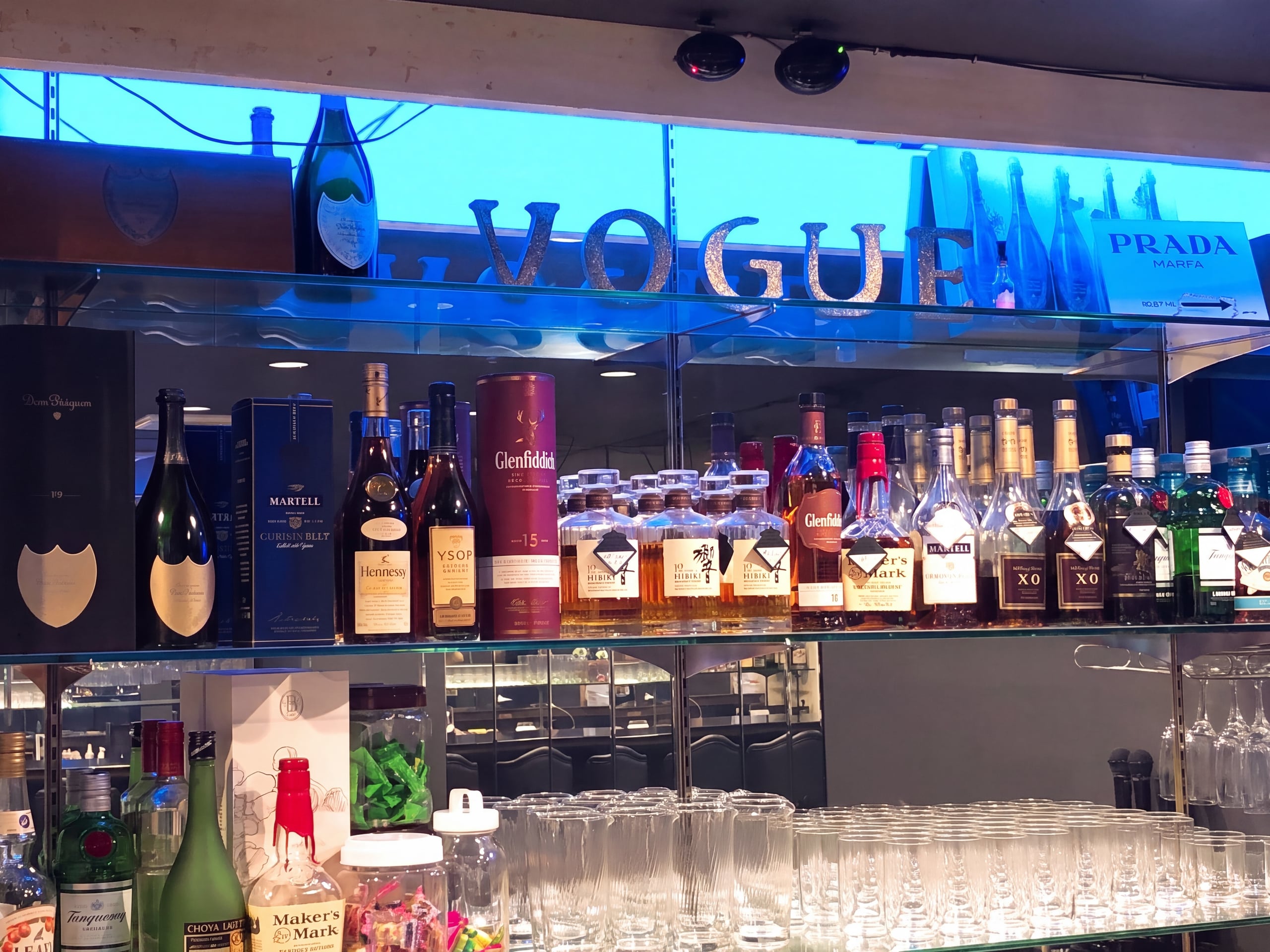 青いネオンに照らされたボトル棚と VOGUE のサイン